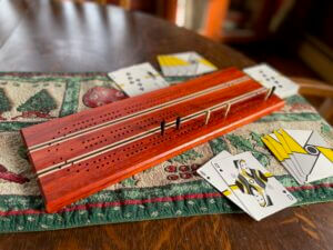 A cribbage board and cards. The board is made of reddish padauk, nearly black wenge and maple. The cards are have spiraled backs in yellow, grey and white with a black circle in the center.