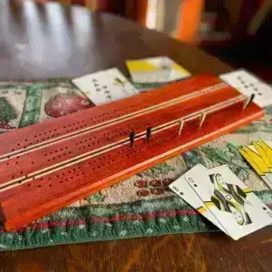 A cribbage board and cards. The board is made of reddish padauk, nearly black wenge and maple. The cards are have spiraled backs in yellow, grey and white with a black circle in the center.
